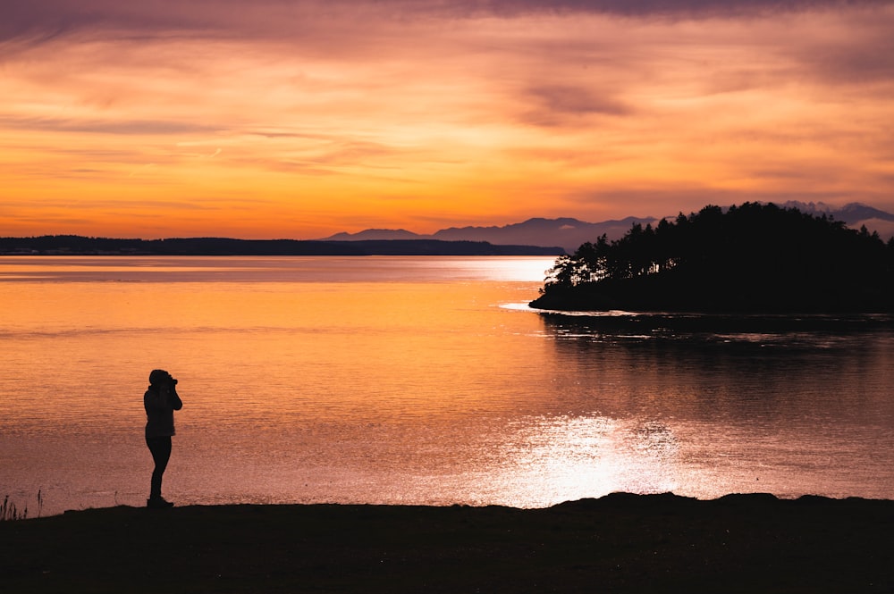 silhouette of man and woman standing beside lake during sunset