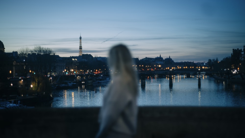 woman in white long sleeve shirt standing near body of water during night time