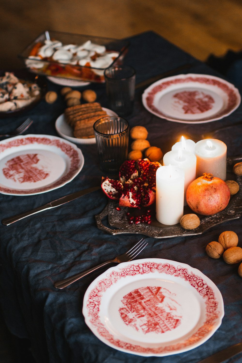 Piatto in ceramica bianca e rossa con forchetta in acciaio inox accanto a biscotti marroni e candele bianche