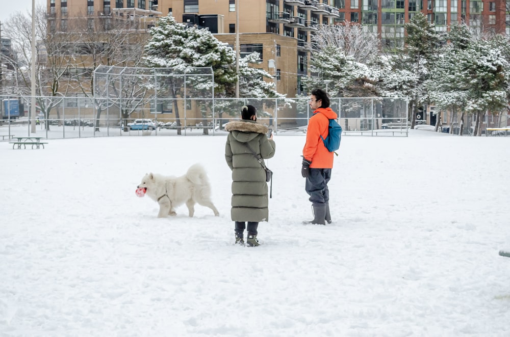 man in brown coat standing on snow covered ground with white dog during daytime