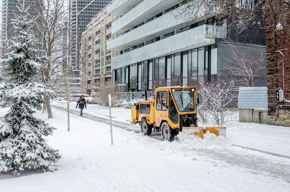 gelbes und schwarzes schweres Gerät tagsüber auf schneebedecktem Boden in der Nähe von Gebäuden