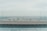 A panoramic view of a cityscape is visible through a transparent glass barrier at the edge of a rooftop. The skyline showcases numerous buildings under a clear, pale sky, suggesting an overcast day.