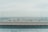 A panoramic view of a cityscape is visible through a transparent glass barrier at the edge of a rooftop. The skyline showcases numerous buildings under a clear, pale sky, suggesting an overcast day.