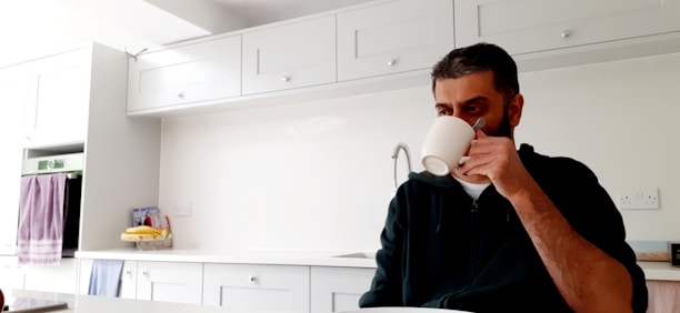 Smiling customer enjoying a glass of milk in a bright kitchen.
