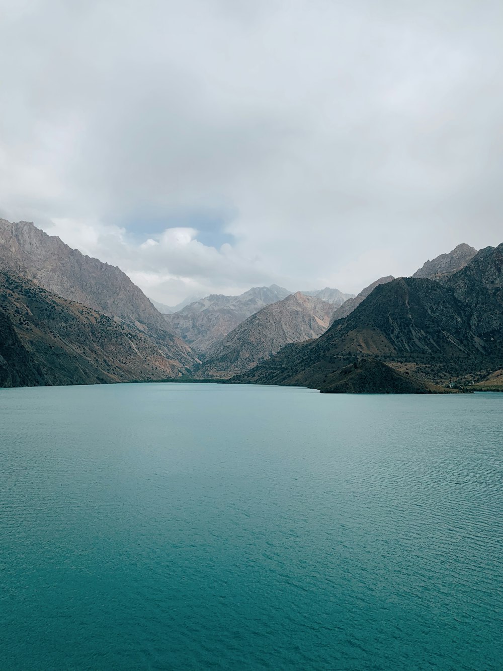 body of water near mountain under cloudy sky during daytime