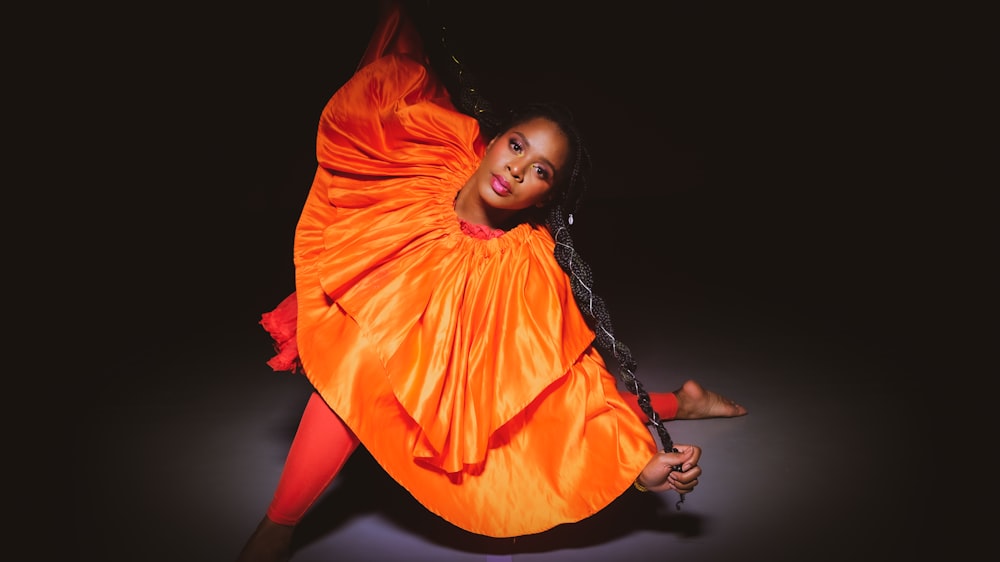 woman in orange dress lying on black background