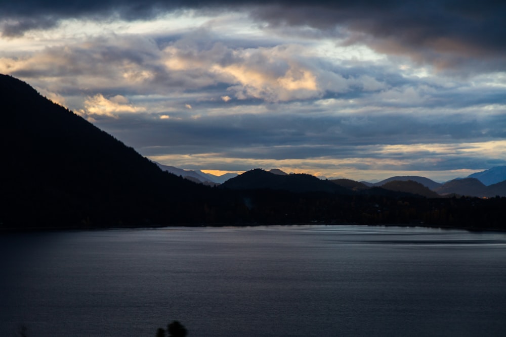 body of water near mountain under cloudy sky during daytime