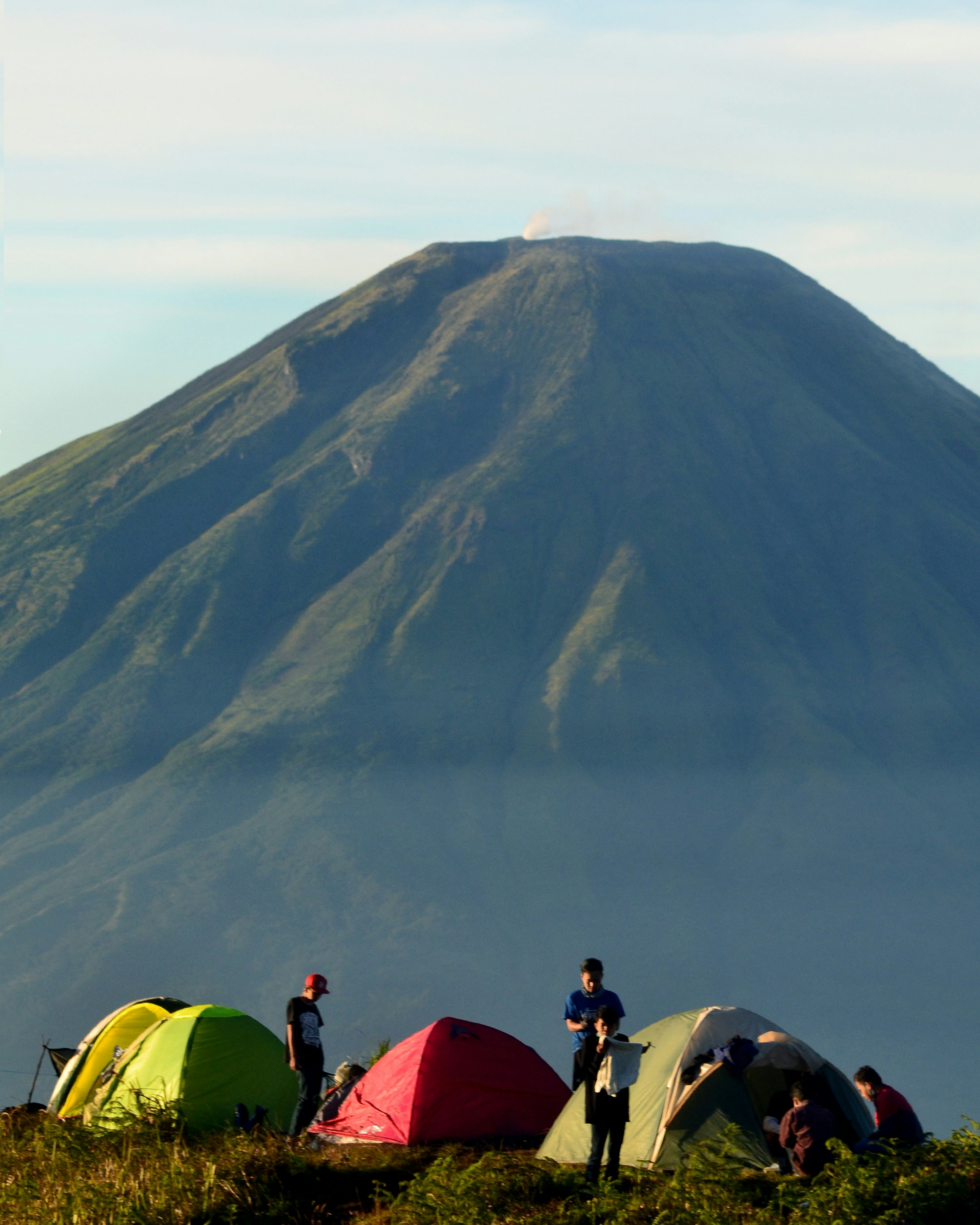 Orang-orang duduk di tenda kubah hijau dekat gunung di siang hari