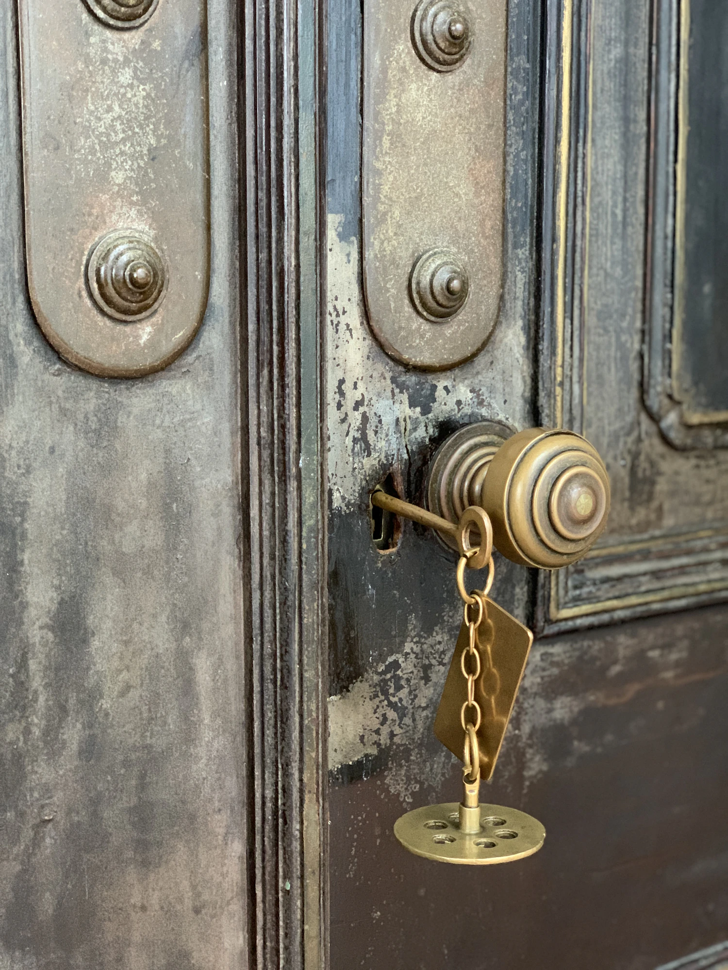 A brass key with a tag left hanging in the lock of a weathered painted door