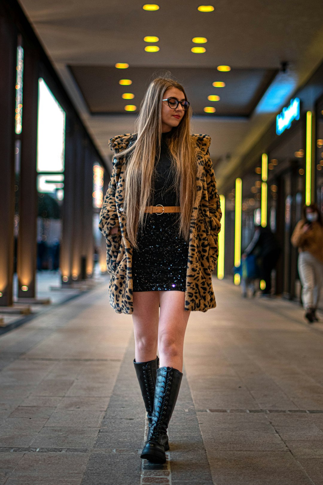 woman in brown leopard coat and black leather boots walking on sidewalk during daytime