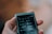 A person holds a small, portable Sony device, likely a music player, with a screen displaying an interface in a language that could be Chinese. The device has several options visible such as music, playlists, and more, indicating its function as a media player. The background is blurred and the focus is on the device.