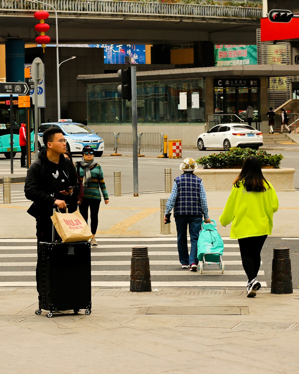 woman in black jacket and green pants holding black bag walking on sidewalk during daytime