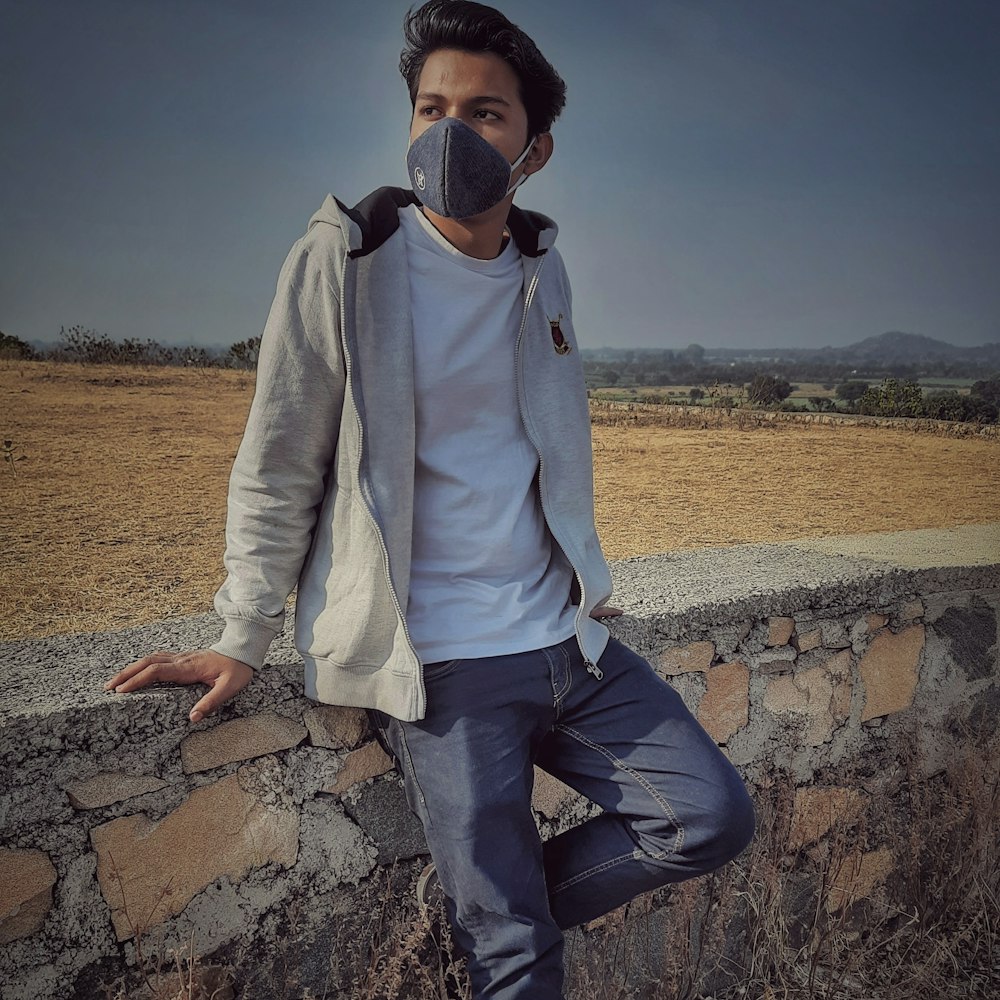 man in white jacket and black pants sitting on rock