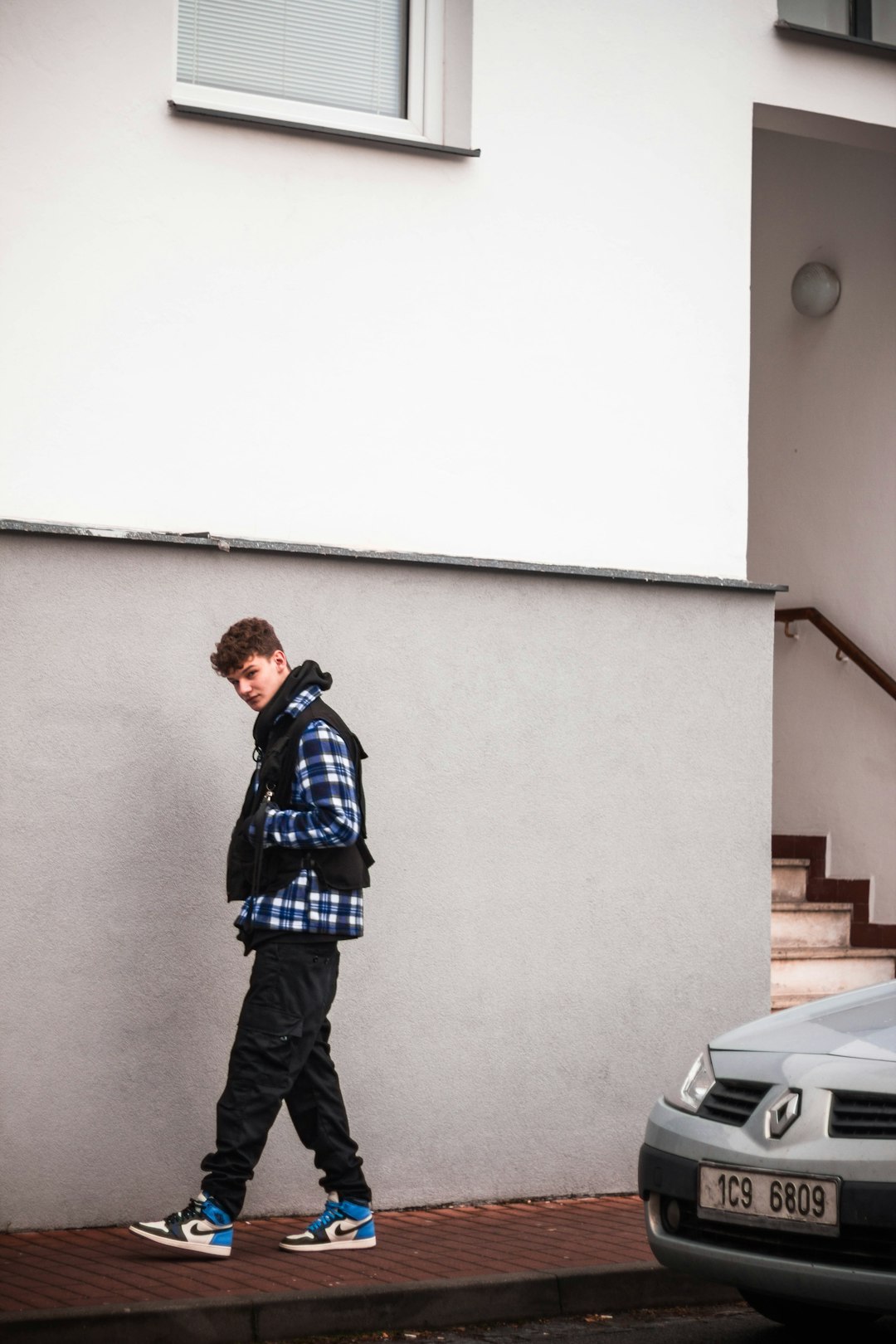 man in blue and white plaid dress shirt and black pants standing near white wall