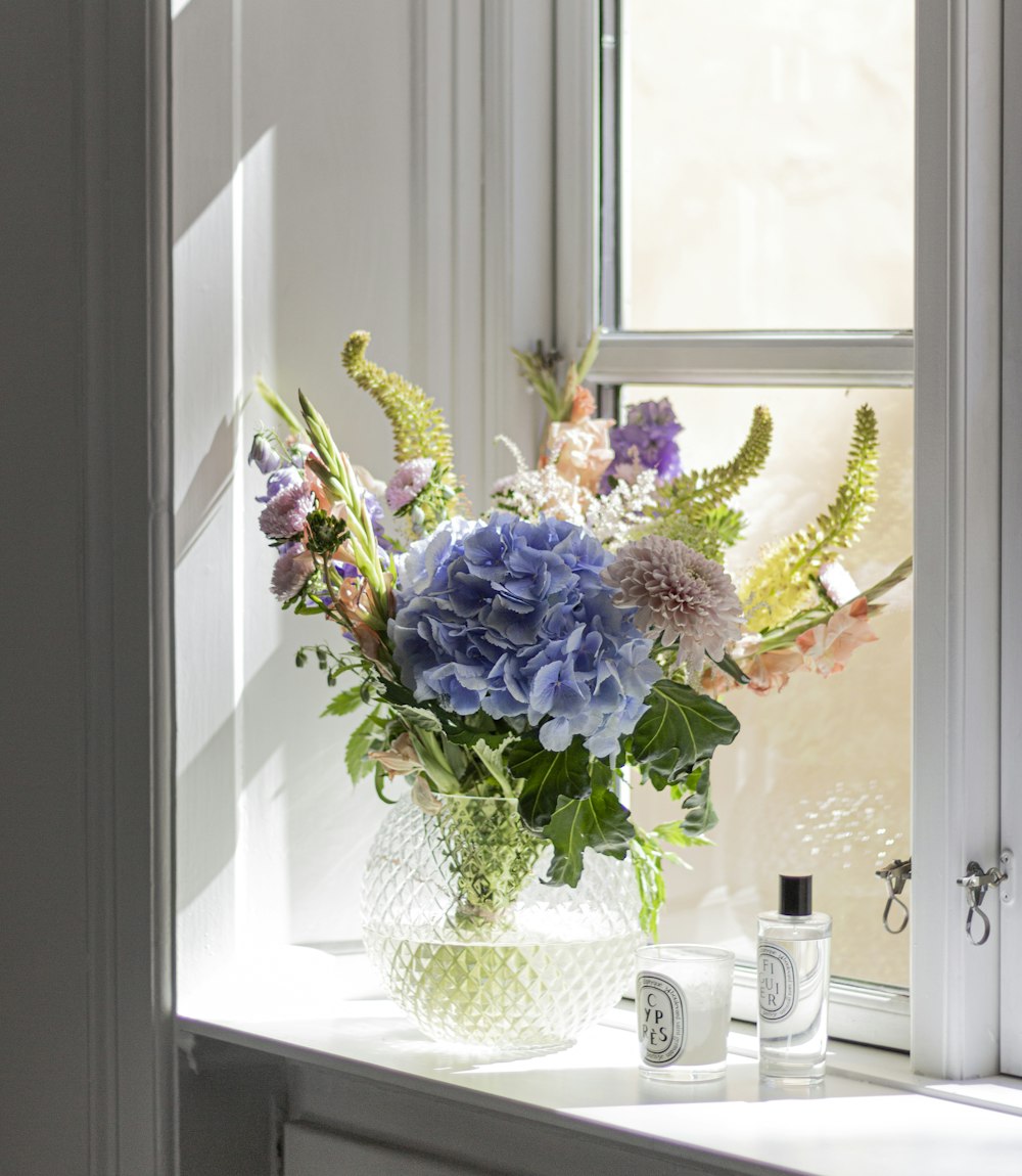 purple and white flowers in white ceramic vase beside window