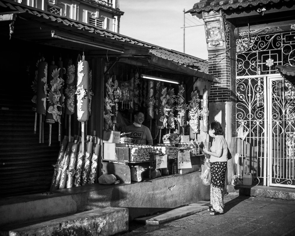 grayscale photo of woman in floral dress standing on sidewalk