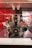 A high-performance engine is displayed on a platform, showcasing its complex mechanical components. The engine appears to be a V12 configuration with a mix of metal parts, belts, and pulleys. The backdrop features a red and black pattern, contributing to a modern and technical ambiance.