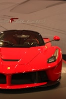A sleek and shiny red sports car with distinctive features and a prominent emblem on the hood. The background showcases an abstract design with the brand name subtly displayed.