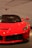 A sleek and shiny red sports car with distinctive features and a prominent emblem on the hood. The background showcases an abstract design with the brand name subtly displayed.
