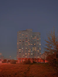 A stately residential building at dusk, illuminated warmly against a deep green and gold sky.