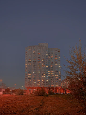 A stately residential building at dusk, illuminated warmly against a deep green and gold sky.