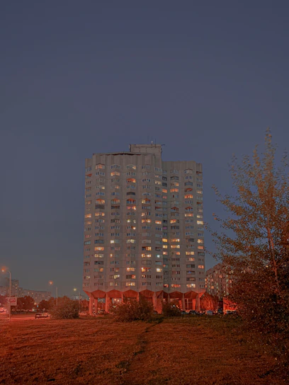 A sleek high-rise residential building on Golf Course Road at sunset, with warm lights glowing from the windows.