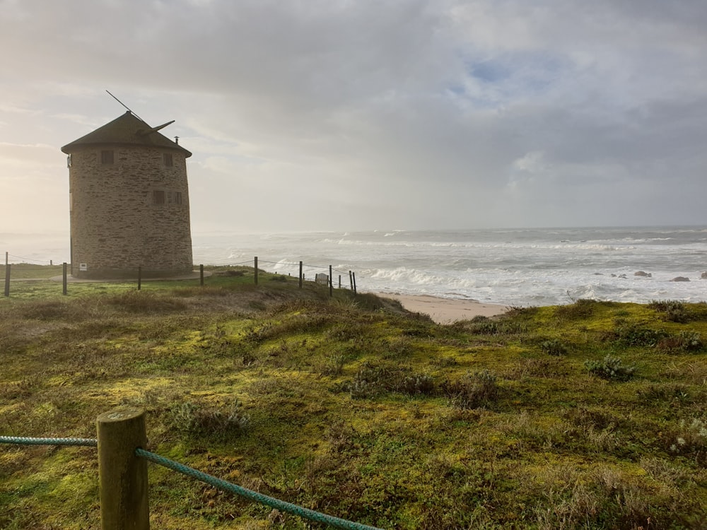 brown concrete building on green grass field near sea under white clouds during daytime