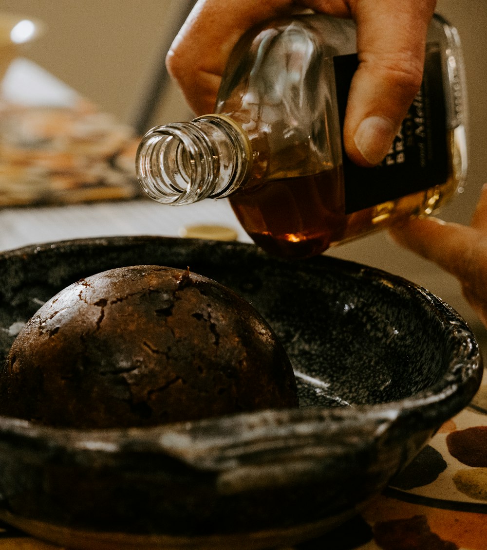 person pouring brown liquid on black ceramic bowl