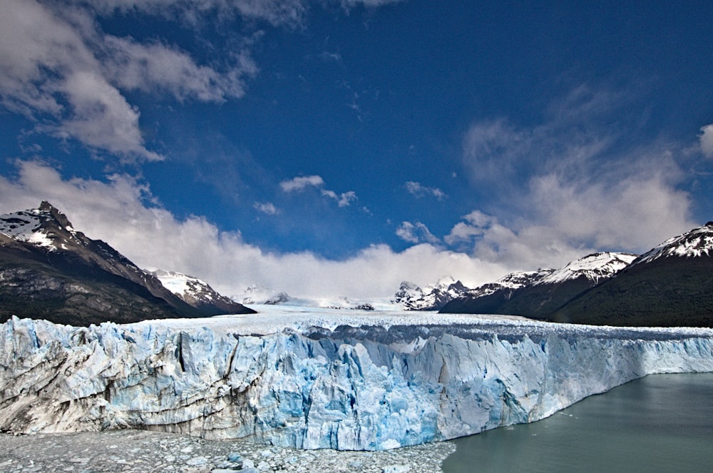 montanha coberta de neve branca perto do corpo de água sob o céu azul durante o dia