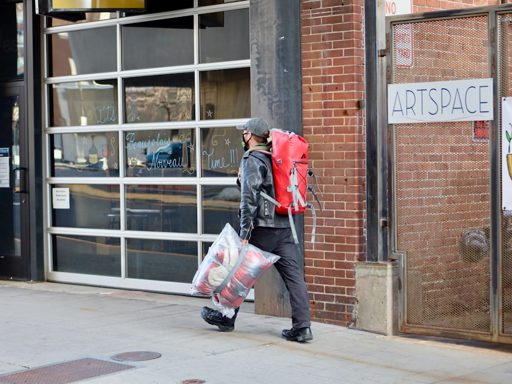 man in red jacket carrying white and pink backpack walking on sidewalk during daytime