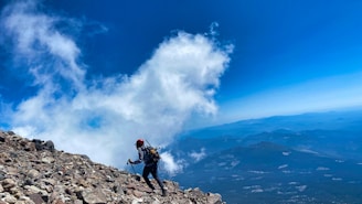 man in black jacket and blue denim jeans standing on rock formation under blue and white