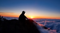 silhouette of man sitting on rock during sunset