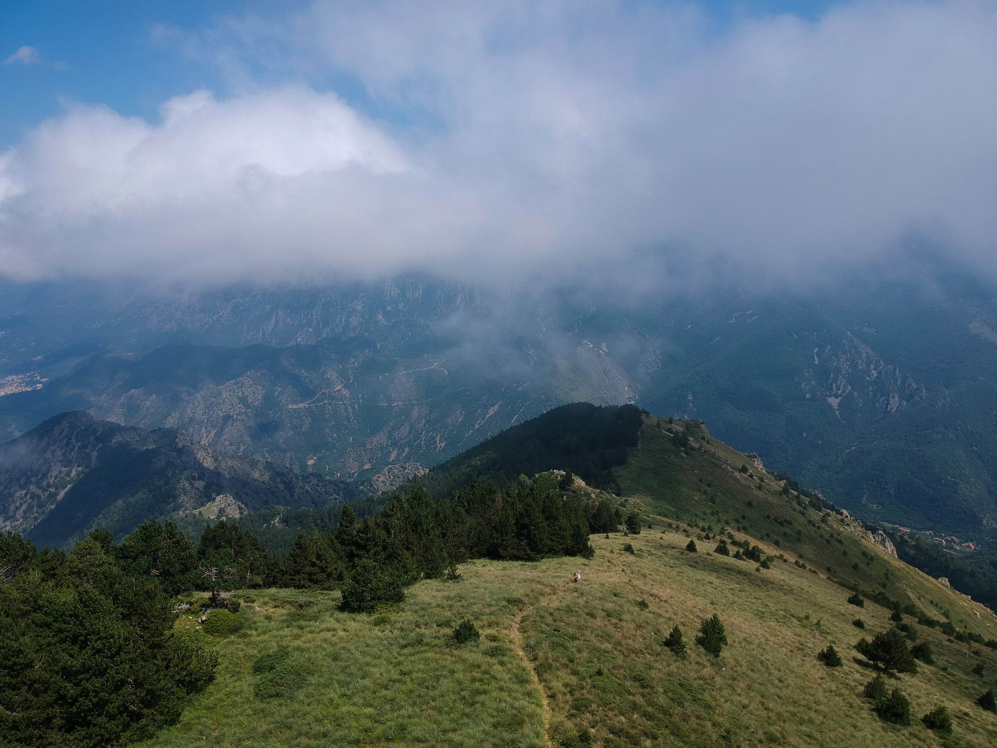campo di erba verde e montagna sotto nuvole bianche e cielo blu durante il giorno