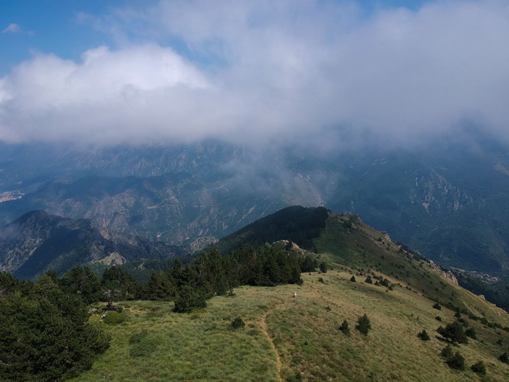 green grass field and mountain under white clouds and blue sky during daytime