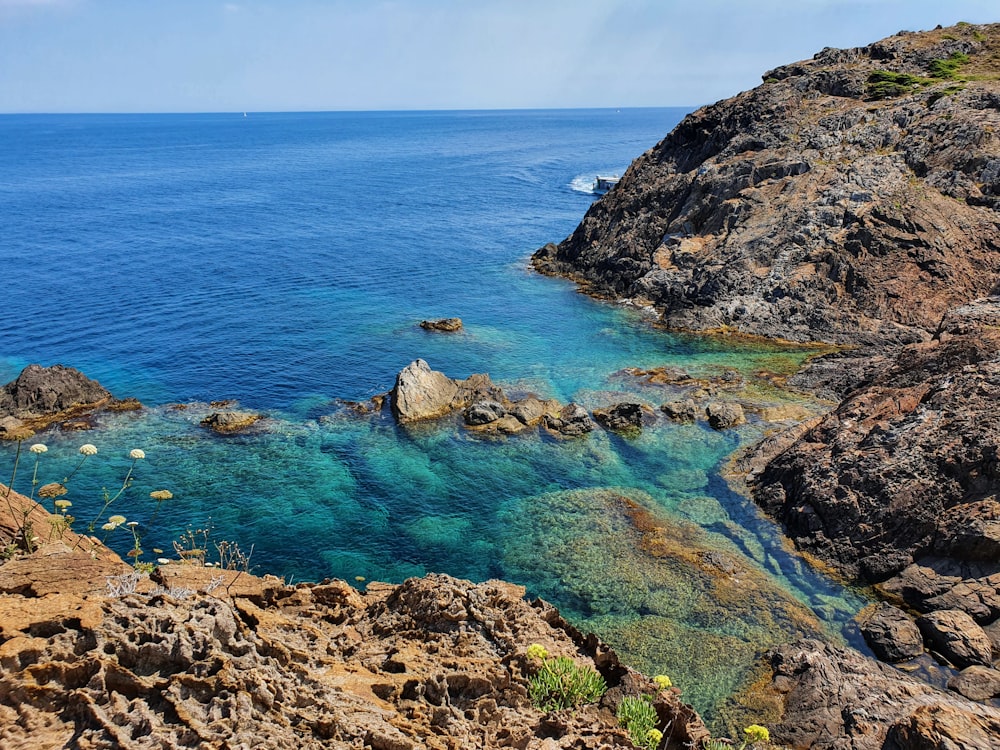 brown and green rock formation beside blue sea under blue sky during daytime