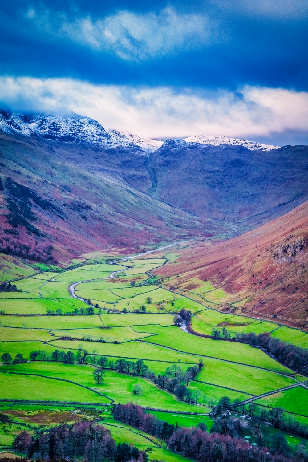 green grass field near mountain under white clouds during daytime