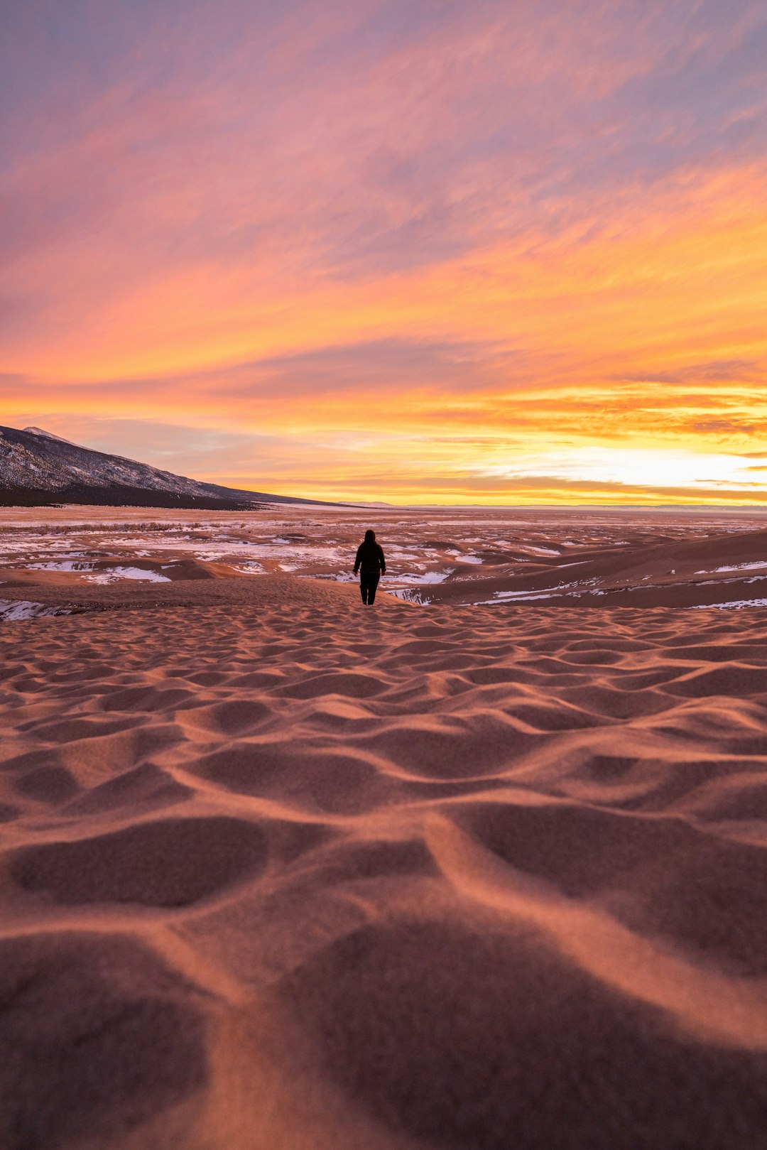 person walking on brown sand during sunset