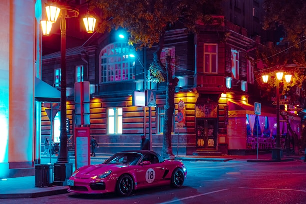 A vibrant night shot of a neon-lit car show with synth pop inspired lighting and dark cityscape.