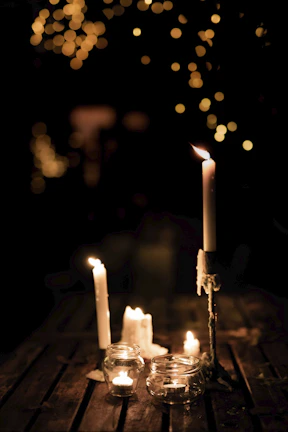 Several handmade candles arranged on a rustic wooden table, their flames reflecting warmth.