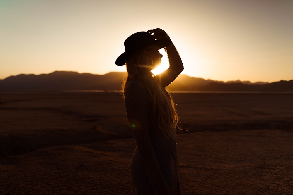 woman in white shirt and black hat standing on beach during sunset