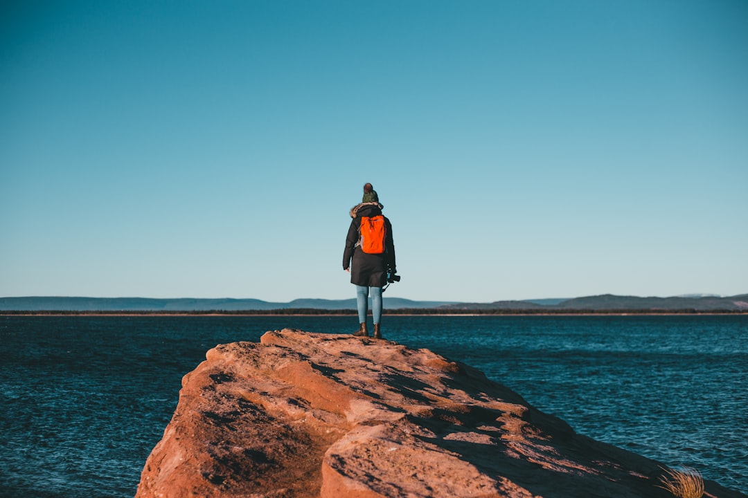 woman in black jacket standing on brown rock formation near body of water during daytime