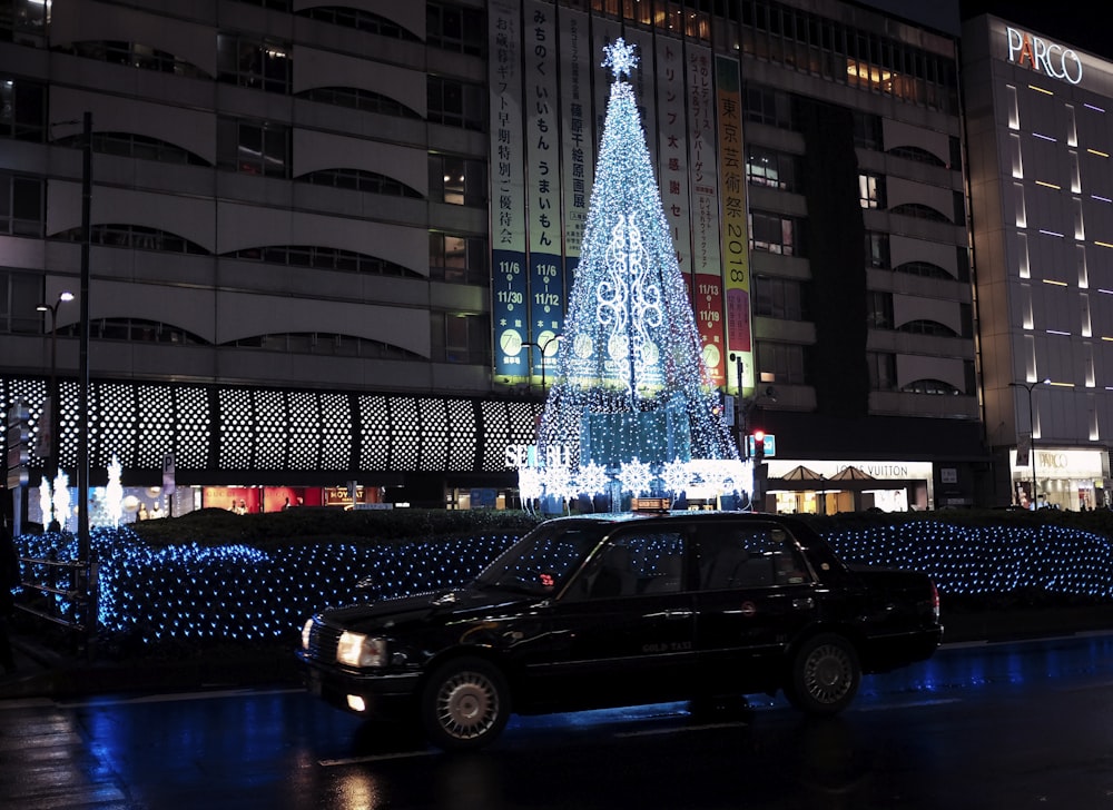 夜間にライトアップされたクリスマスツリーの近くに駐車された黒いセダン