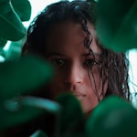 girl in white shirt behind green leaves during daytime