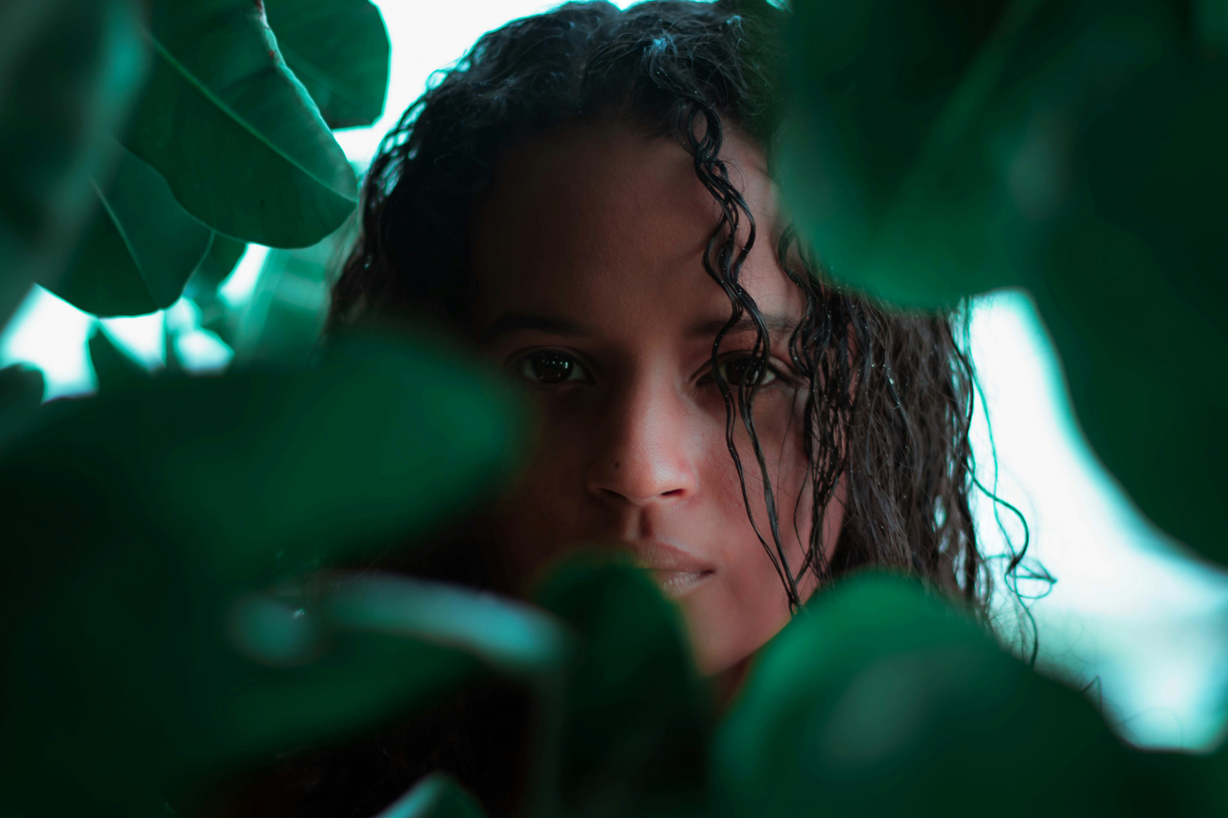 girl in white shirt behind green leaves during daytime