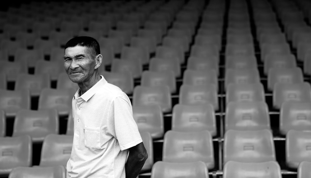 grayscale photo of man in white button up shirt standing on chair