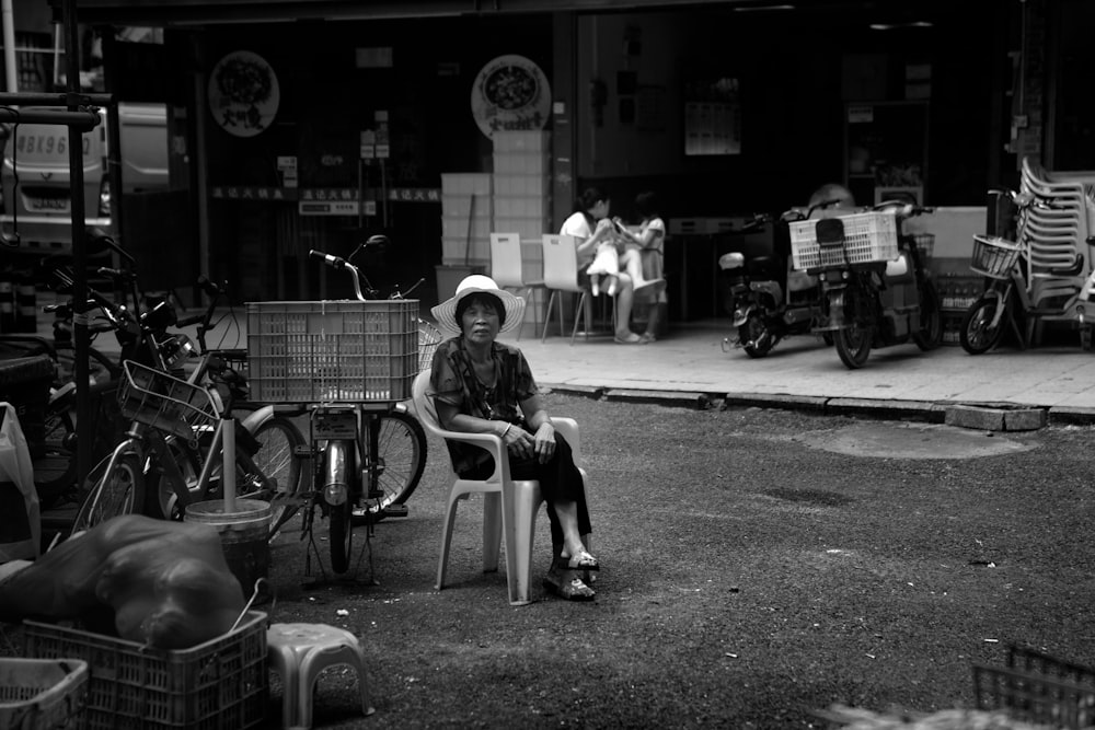 grayscale photo of man sitting on chair near motorcycle