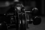 A close-up, black and white image of a string instrument's tuning pegs and scroll. The focus is on the wood's texture and the curves of the instrument.