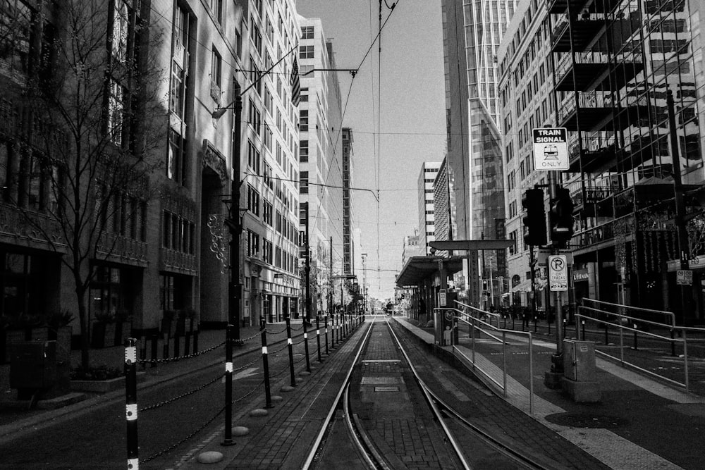 grayscale photo of train rail between buildings
