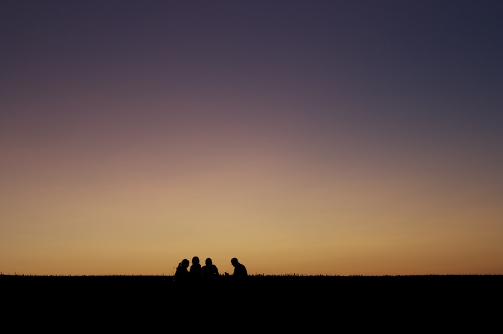 silhouette of people sitting on ground during sunset