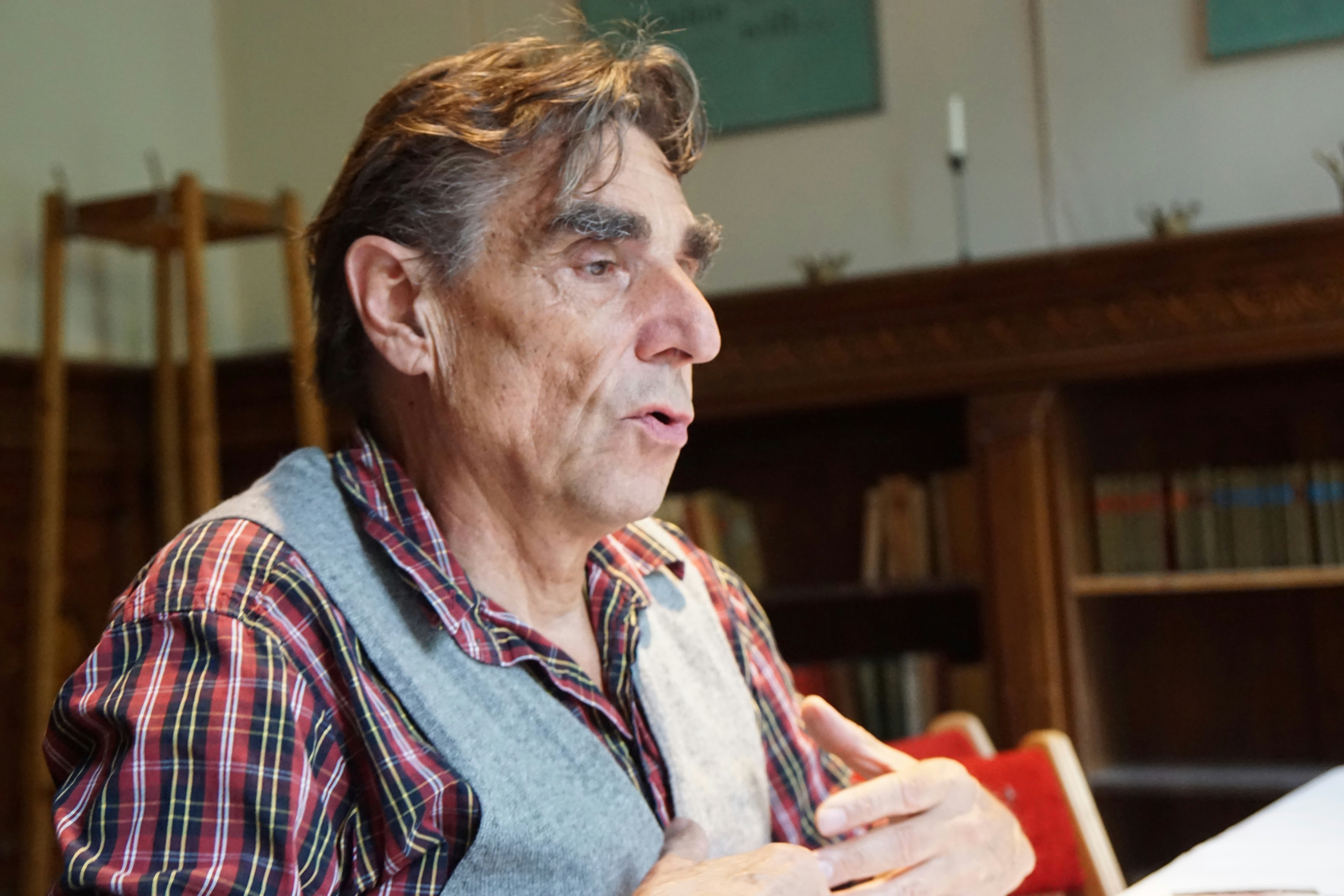 man in red white and black plaid dress shirt, Portrait of a visionary man. Tousled hair, bushy eyebrows, expressive hands, looking down in recollection.